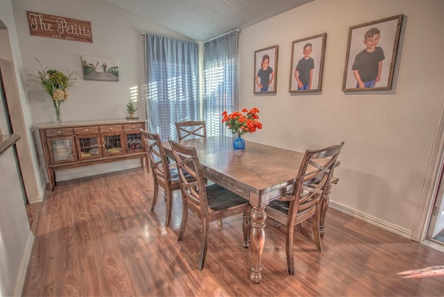 dining space featuring hardwood / wood-style floors, vaulted ceiling, and a textured ceiling