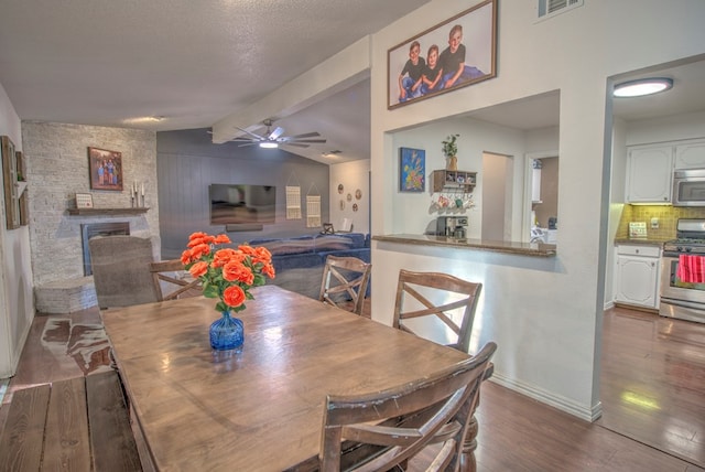 dining area featuring lofted ceiling with beams, a large fireplace, dark hardwood / wood-style flooring, ceiling fan, and a textured ceiling