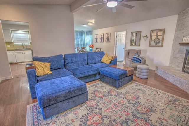 living room with a fireplace, lofted ceiling with beams, wood-type flooring, sink, and a textured ceiling