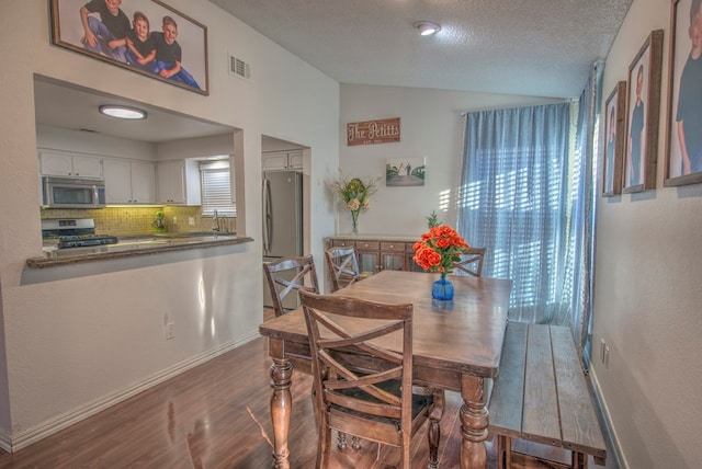 dining area featuring sink, dark wood-type flooring, vaulted ceiling, and a textured ceiling