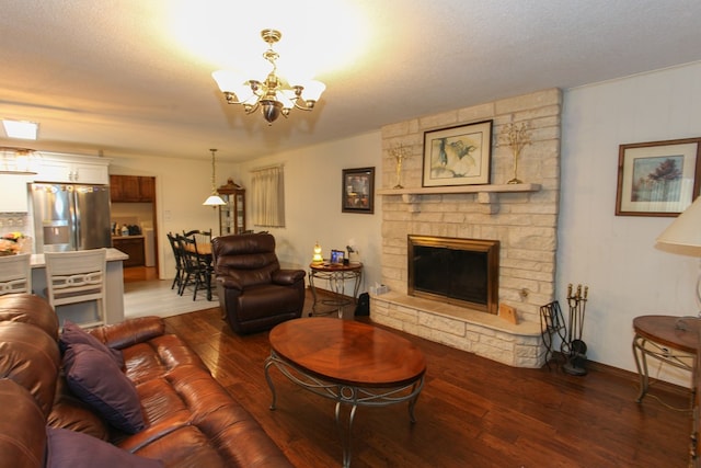 living area featuring baseboards, dark wood-style floors, a stone fireplace, and a notable chandelier