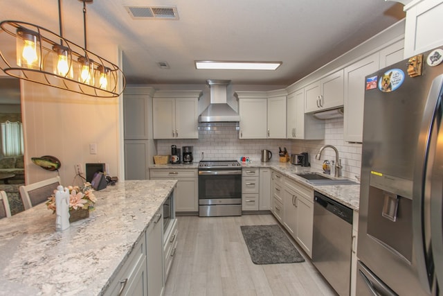 kitchen with visible vents, a sink, wall chimney exhaust hood, light wood-style floors, and appliances with stainless steel finishes