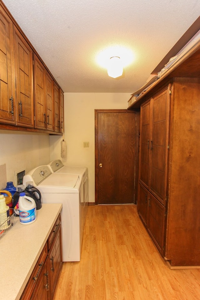 washroom with cabinet space, washing machine and dryer, light wood-type flooring, and a textured ceiling