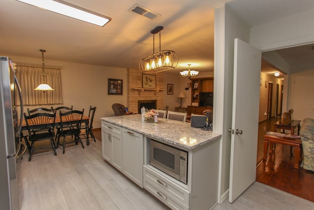 kitchen with light stone counters, visible vents, light wood-style floors, stainless steel appliances, and a fireplace