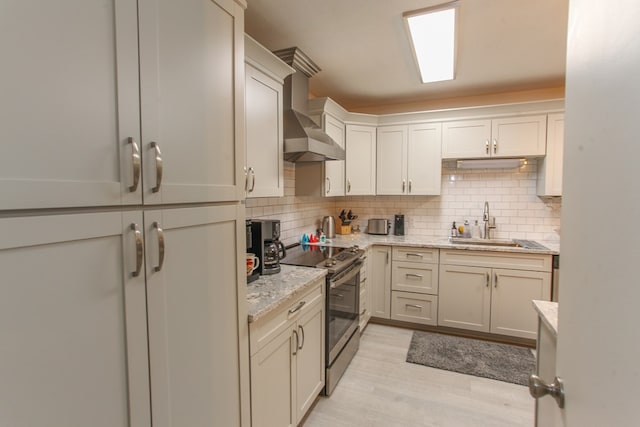 kitchen with a sink, wall chimney range hood, tasteful backsplash, light wood finished floors, and electric stove