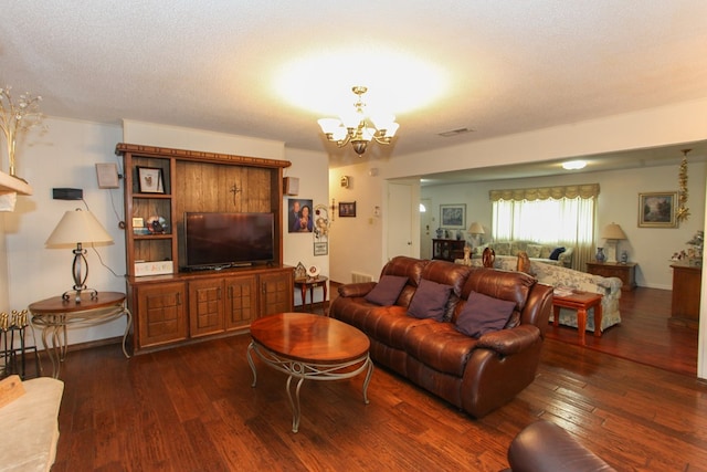 living room featuring a textured ceiling, a notable chandelier, visible vents, and dark wood-style floors