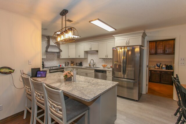 kitchen with light wood-style flooring, a sink, wall chimney exhaust hood, stainless steel appliances, and light stone counters