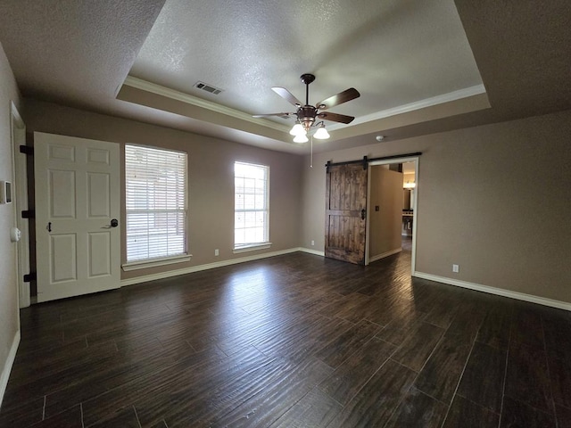 empty room with a barn door, ceiling fan, dark hardwood / wood-style floors, a raised ceiling, and a textured ceiling