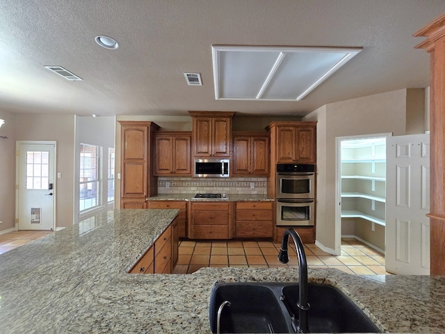 kitchen featuring decorative backsplash, sink, light stone countertops, stainless steel appliances, and light tile patterned floors