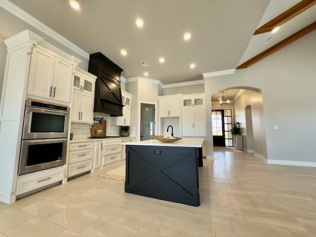 5516 E County Rd 93, Midland, TX 79706 - kitchen with double oven, arched walkways, custom exhaust hood, ornamental molding, and an island with sink