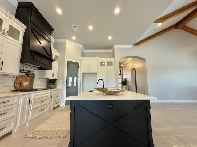5516 E County Rd 93, Midland, TX 79706 - kitchen with arched walkways, a center island with sink, backsplash, white cabinetry, and ornamental molding