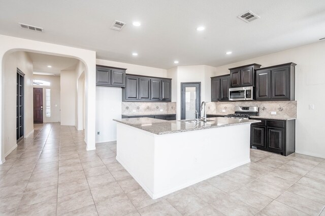 4906 Meadowside St, Midland, TX 79705 - kitchen with appliances with stainless steel finishes, arched walkways, a center island with sink, decorative backsplash, and recessed lighting
