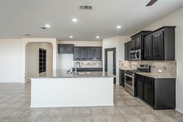 4906 Meadowside St, Midland, TX 79705 - kitchen featuring stainless steel appliances, arched walkways, light stone counters, a kitchen island with sink, and tasteful backsplash