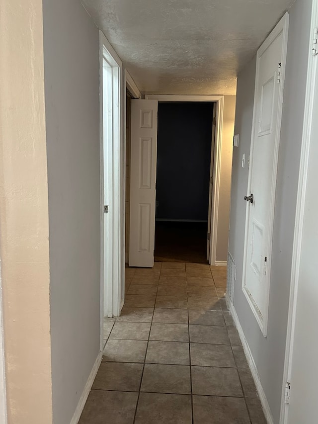 hallway with a textured ceiling and tile patterned floors