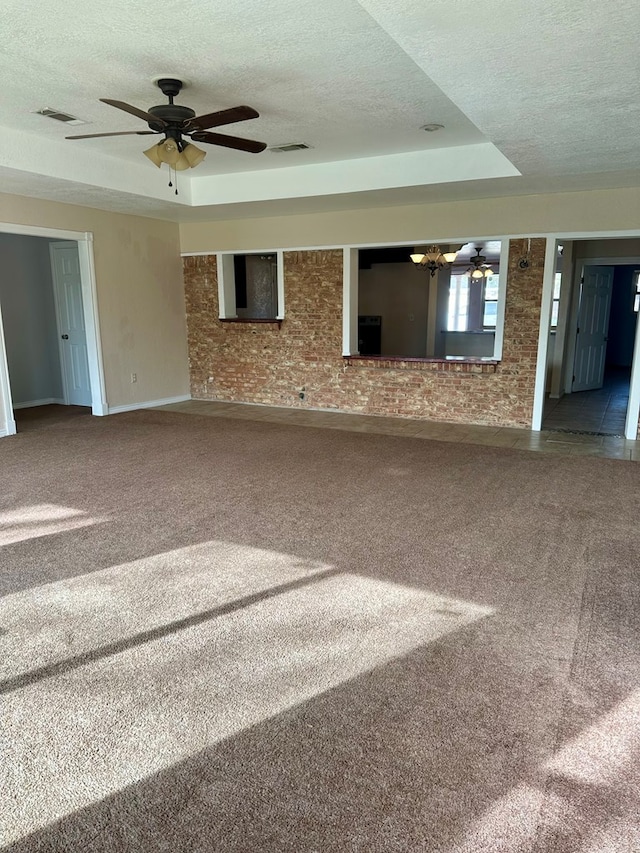 carpeted spare room featuring a raised ceiling, ceiling fan, brick wall, and a textured ceiling