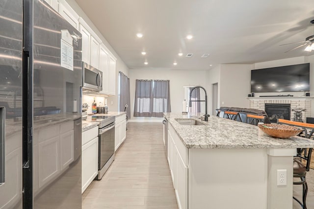 6909 Moonlight, Midland, TX 79705 - kitchen featuring a sink, a brick fireplace, a kitchen island with sink, ceiling fan, and appliances with stainless steel finishes