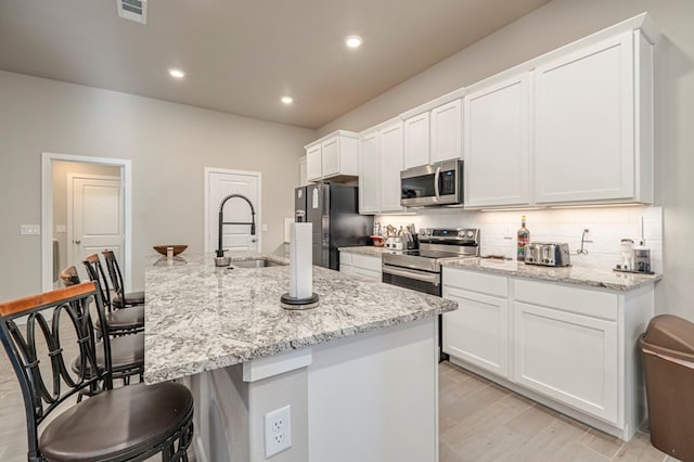 6909 Moonlight, Midland, TX 79705 - kitchen featuring a breakfast bar, a sink, white cabinetry, visible vents, and appliances with stainless steel finishes