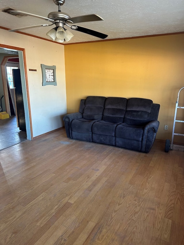 living room featuring ceiling fan, ornamental molding, a textured ceiling, and light wood-type flooring