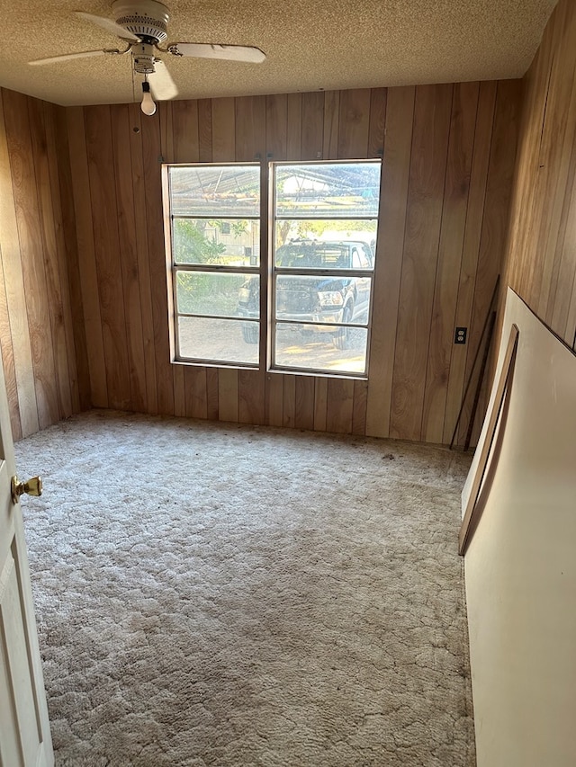 carpeted empty room featuring a textured ceiling, ceiling fan, and wood walls