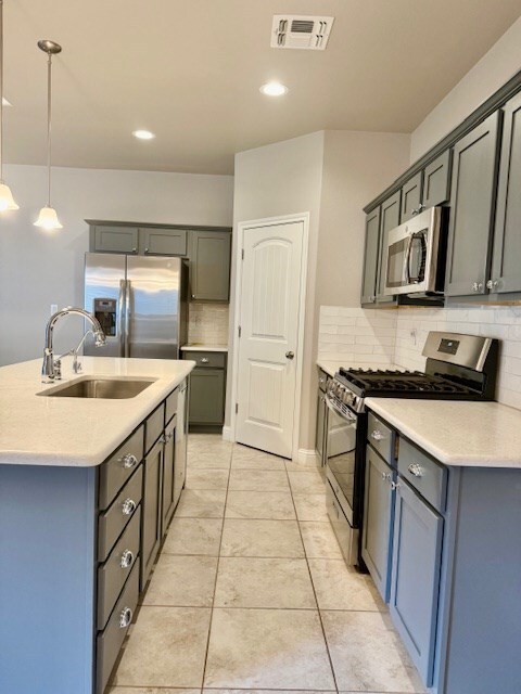 37 Devon Ct, Odessa, TX 79765 - kitchen featuring appliances with stainless steel finishes, tasteful backsplash, a kitchen island with sink, pendant lighting, and light countertops
