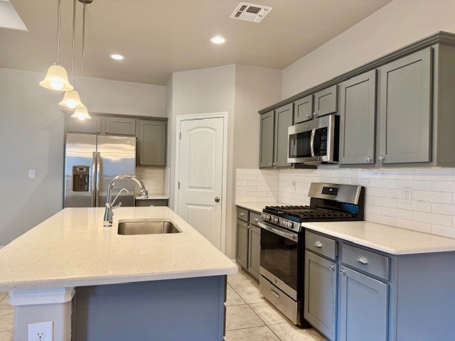 37 Devon Ct, Odessa, TX 79765 - kitchen with stainless steel appliances, decorative backsplash, a kitchen island with sink, hanging light fixtures, and gray cabinetry