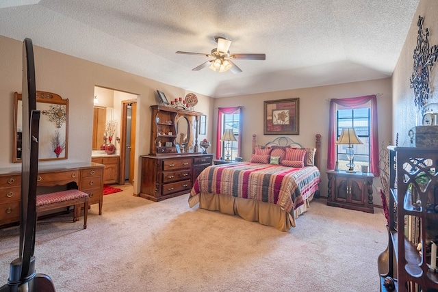 bedroom with ensuite bath, light colored carpet, vaulted ceiling, ceiling fan, and a textured ceiling