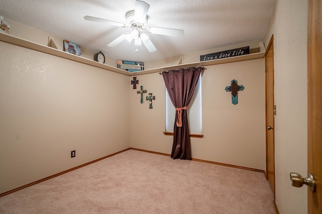 empty room featuring a ceiling fan, baseboards, light colored carpet, and a textured ceiling