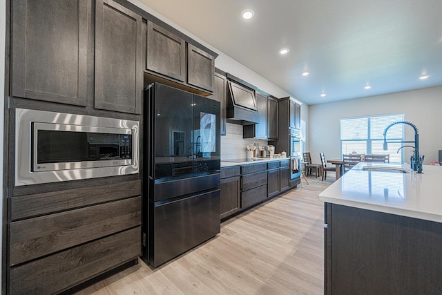 6803 Leather Ln, Midland, TX 79705 - kitchen with stainless steel microwave, a sink, premium range hood, dark brown cabinets, and light wood finished floors