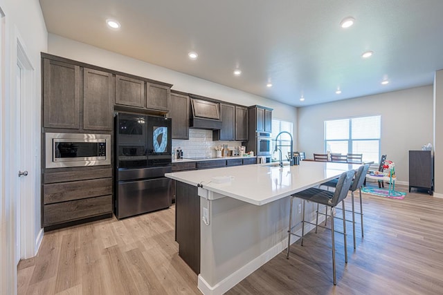 6803 Leather Ln, Midland, TX 79705 - kitchen featuring black appliances, custom exhaust hood, a center island with sink, a kitchen bar, and light wood-style flooring
