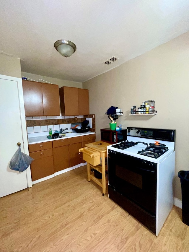 kitchen with white range with gas cooktop, decorative backsplash, and light hardwood / wood-style floors