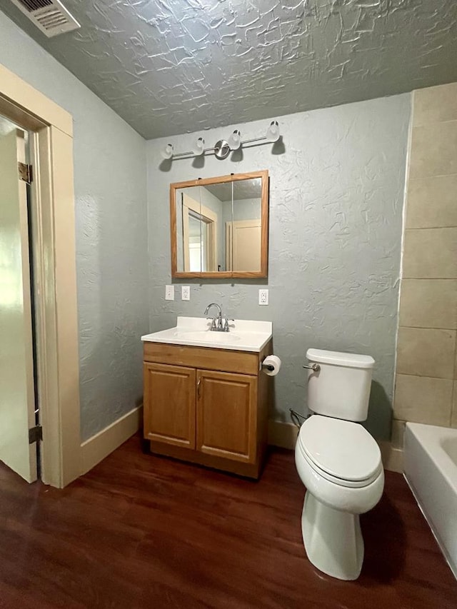 bathroom featuring a washtub, hardwood / wood-style floors, a textured ceiling, toilet, and vanity