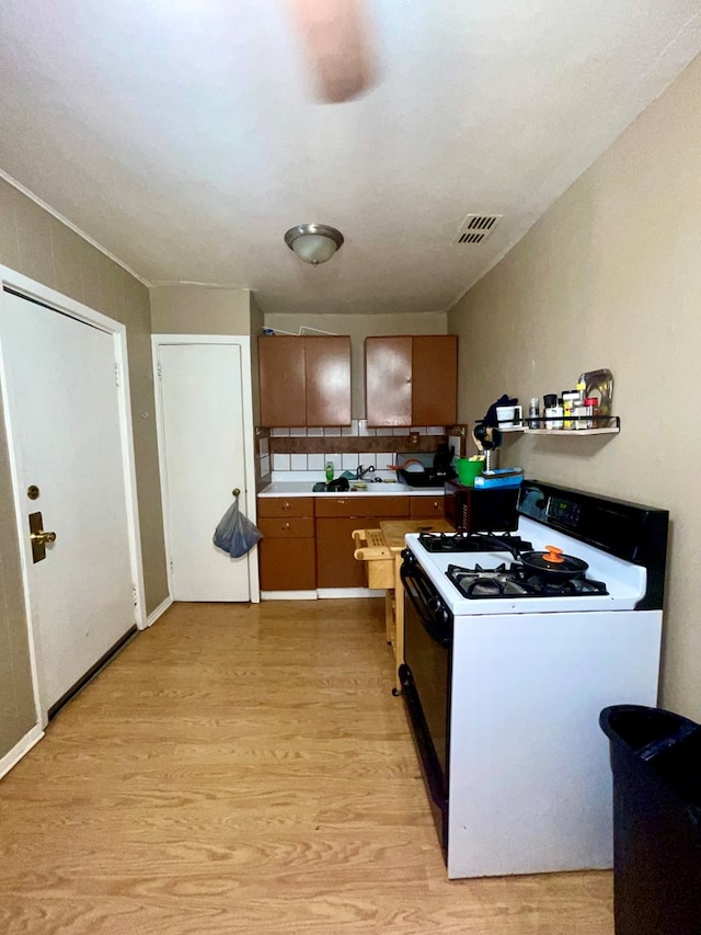 kitchen with white range with gas cooktop, decorative backsplash, light hardwood / wood-style flooring, and sink