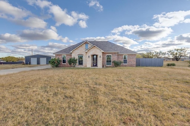 view of front of home featuring a detached garage, an outbuilding, fence, a front lawn, and brick siding