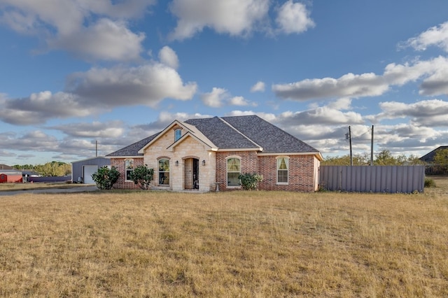 view of front facade with brick siding, a front yard, fence, and a shingled roof