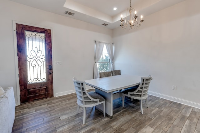 dining area featuring visible vents, baseboards, wood tiled floor, a tray ceiling, and an inviting chandelier