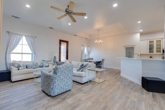 living room with a tray ceiling, visible vents, and plenty of natural light