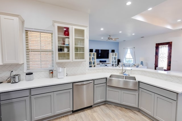 kitchen with dishwasher, backsplash, gray cabinets, light wood-style floors, and a sink