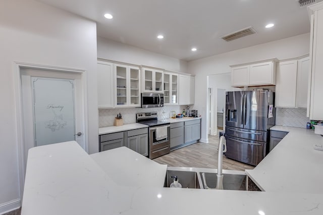 kitchen featuring visible vents, white cabinets, light stone countertops, stainless steel appliances, and a sink