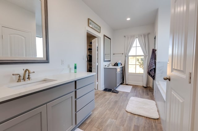 full bath featuring a washtub, recessed lighting, wood finished floors, two vanities, and a sink