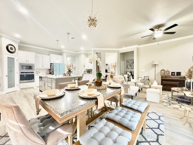 dining room with light wood-style floors, ornamental molding, and ceiling fan with notable chandelier