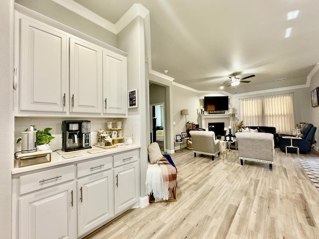 interior space featuring white cabinets, ornamental molding, light wood-type flooring, a fireplace, and backsplash