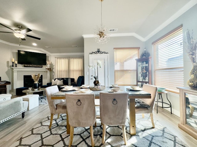 dining room with lofted ceiling, light wood-style flooring, a fireplace, visible vents, and ornamental molding