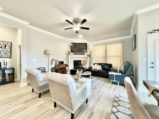 living area with light wood finished floors, visible vents, ceiling fan, crown molding, and a fireplace