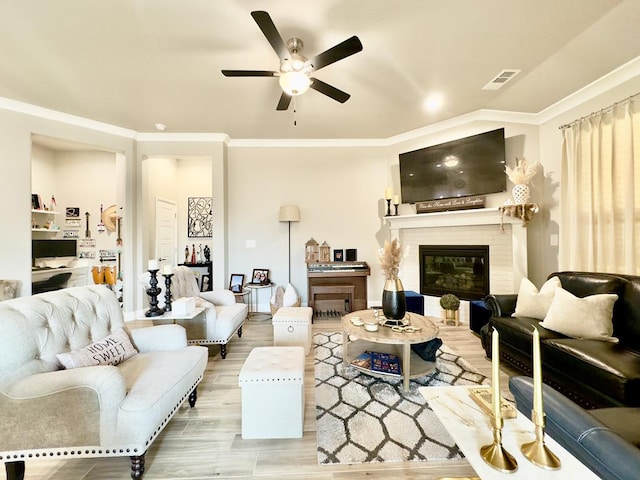 living room with a fireplace, wood finished floors, visible vents, a ceiling fan, and ornamental molding