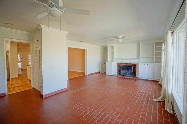 unfurnished living room featuring ceiling fan, crown molding, and a fireplace