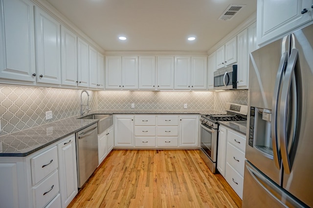 kitchen with stainless steel appliances, white cabinets, decorative backsplash, light hardwood / wood-style floors, and sink