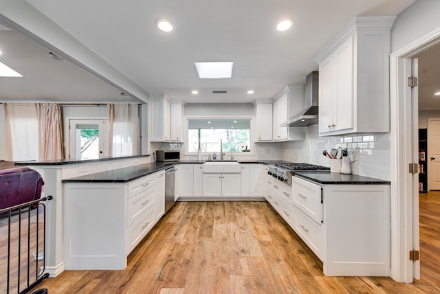2603 Hughes St, Midland, TX 79705 - kitchen with a skylight, wall chimney exhaust hood, stainless steel appliances, a peninsula, and white cabinetry