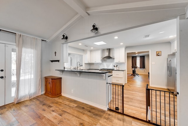 2603 Hughes St, Midland, TX 79705 - kitchen with wall chimney exhaust hood, light wood finished floors, white cabinetry, and a kitchen breakfast bar
