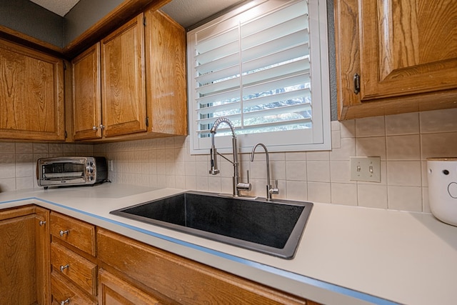 kitchen featuring a sink, brown cabinetry, tasteful backsplash, and light countertops