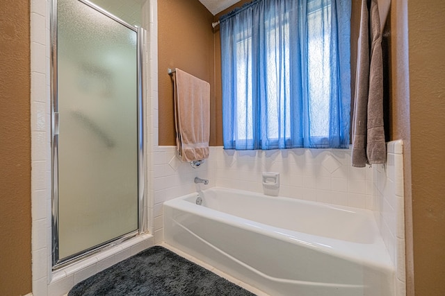 bathroom with a textured wall, a stall shower, and a bath
